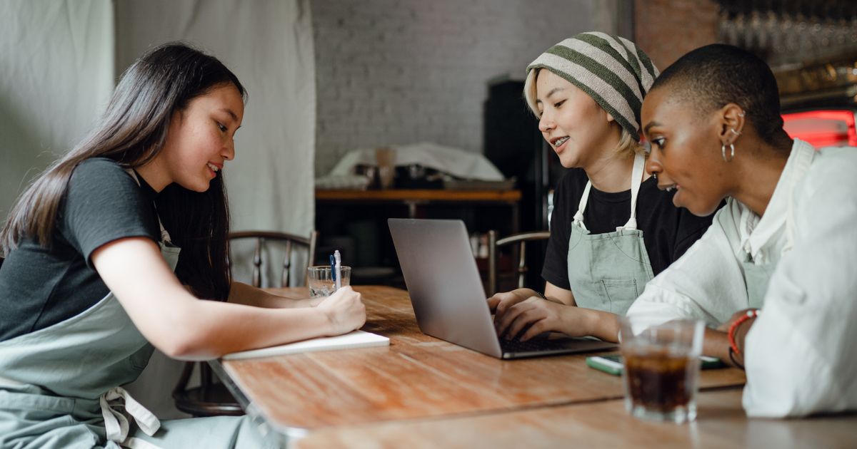 Three small-business owners collaborating around a laptop at a shared table