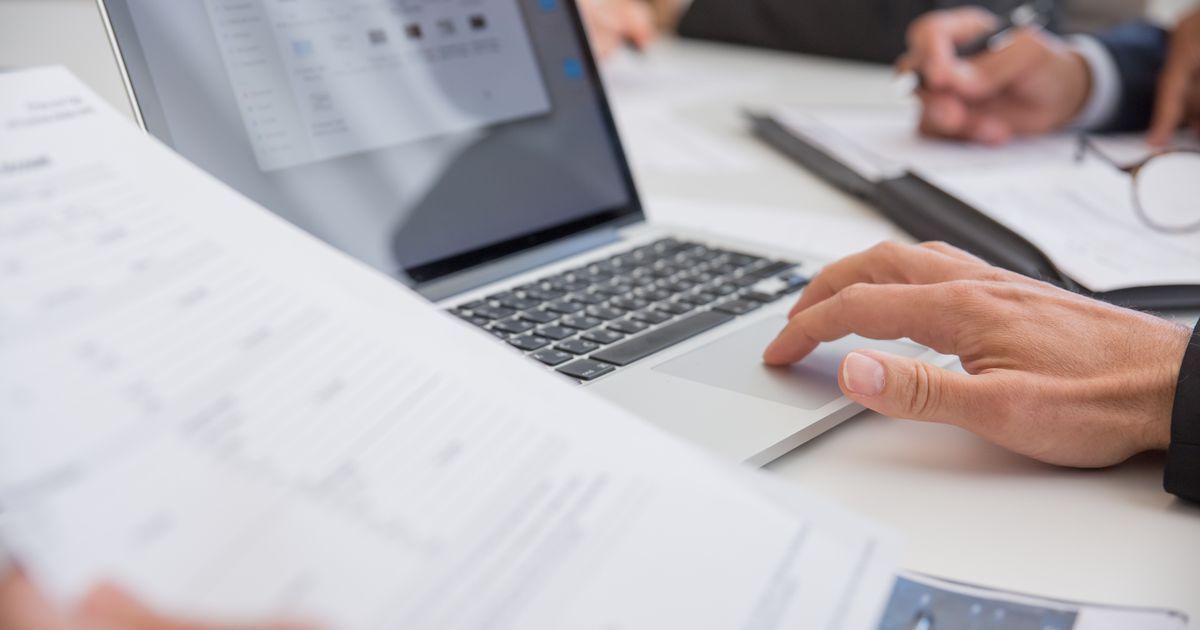 A professional reviewing a document at a laptop before acting, a colleague beside them